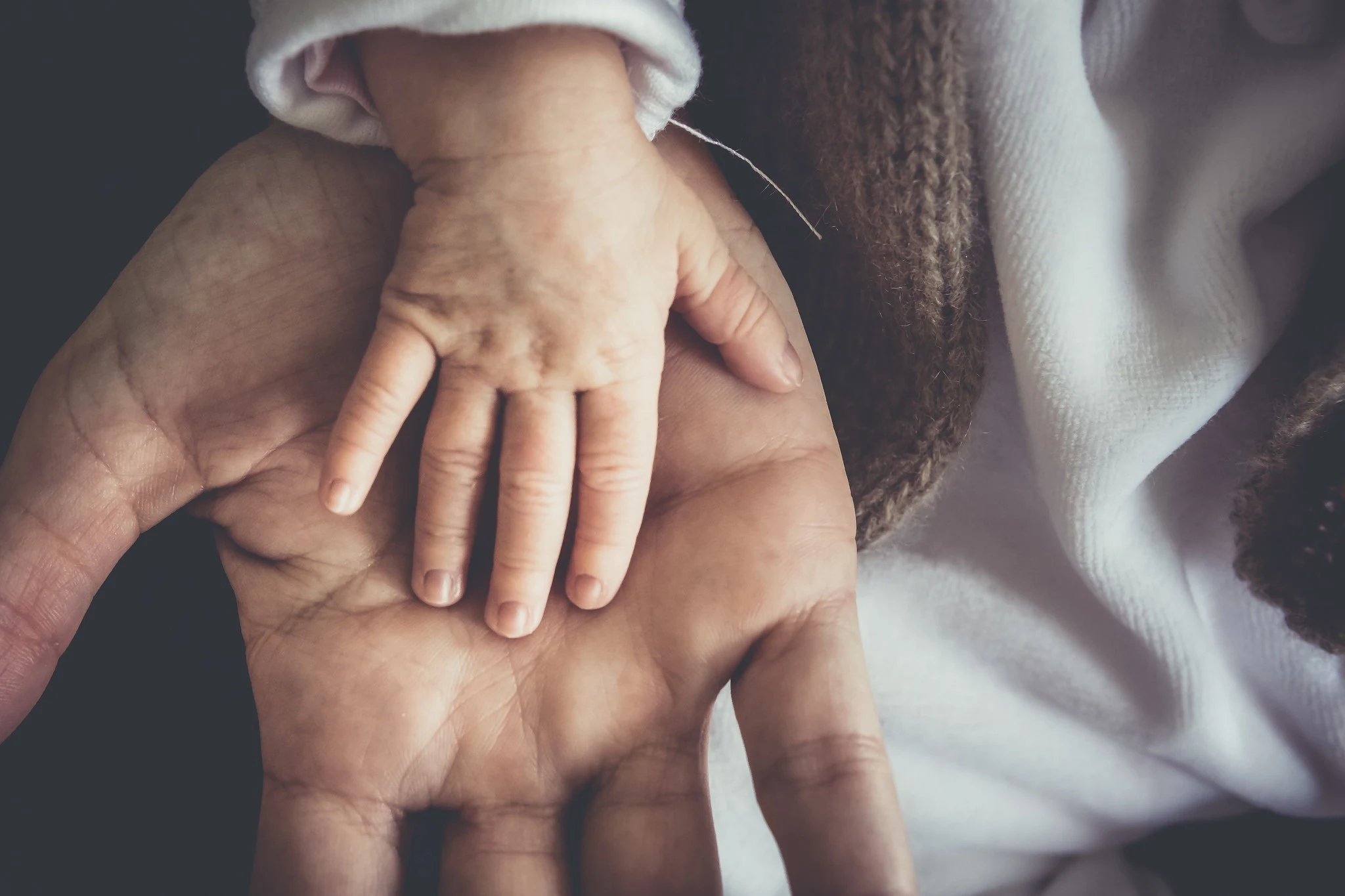 Die winzige Hand eines Säuglings ruht in der geöffneten Handfläche einer erwachsenen Person.